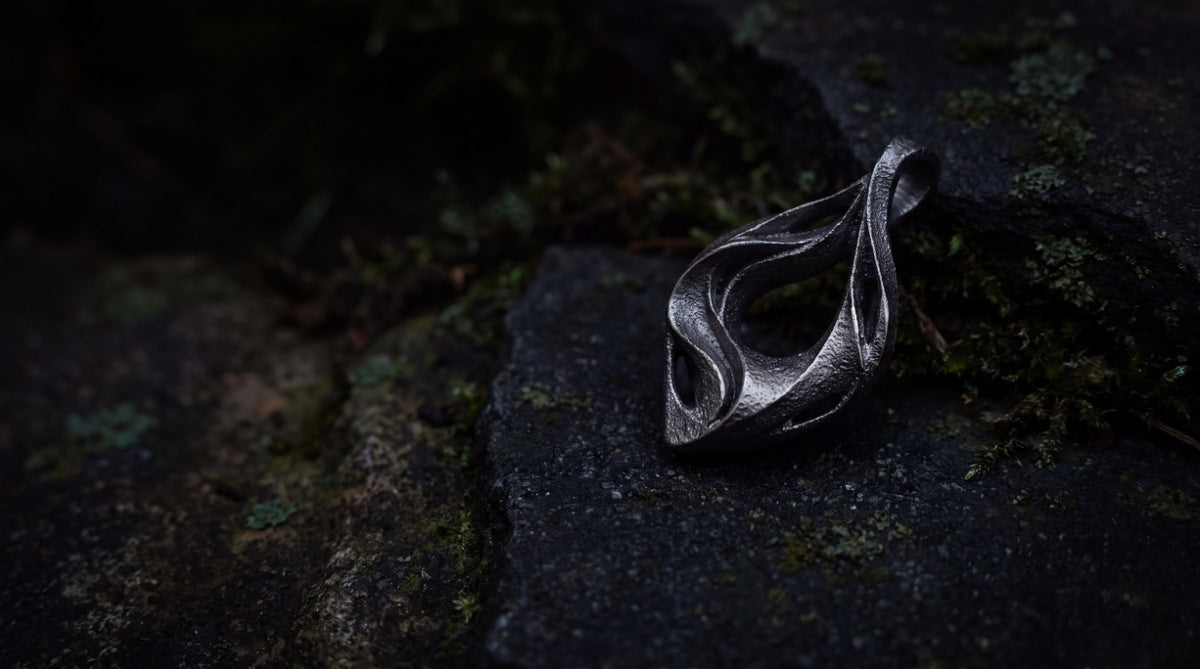 UNDA titanium pendant on dark stone with green moss